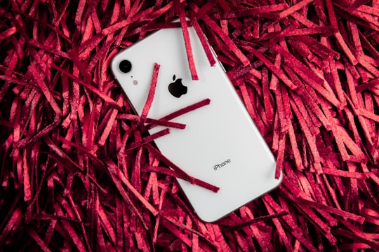 A white smartphone with a prominent logo lies amidst a mass of bright red shredded paper strips.
