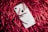 A white smartphone with a prominent logo lies amidst a mass of bright red shredded paper strips.