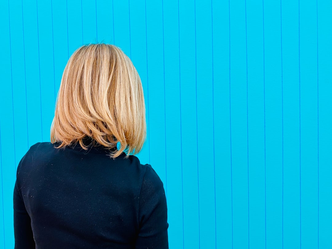 The back of a woman with blond hair on a blue striped background.