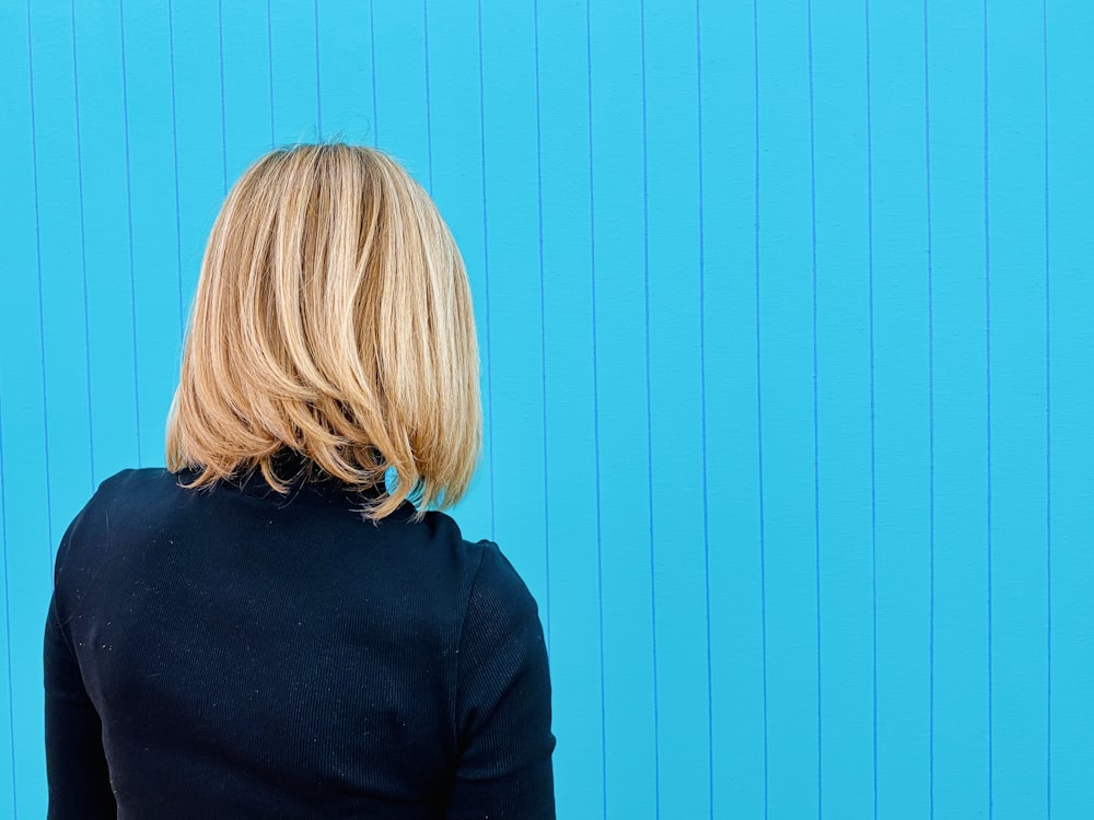 Femme en chemise noire debout près du mur bleu
