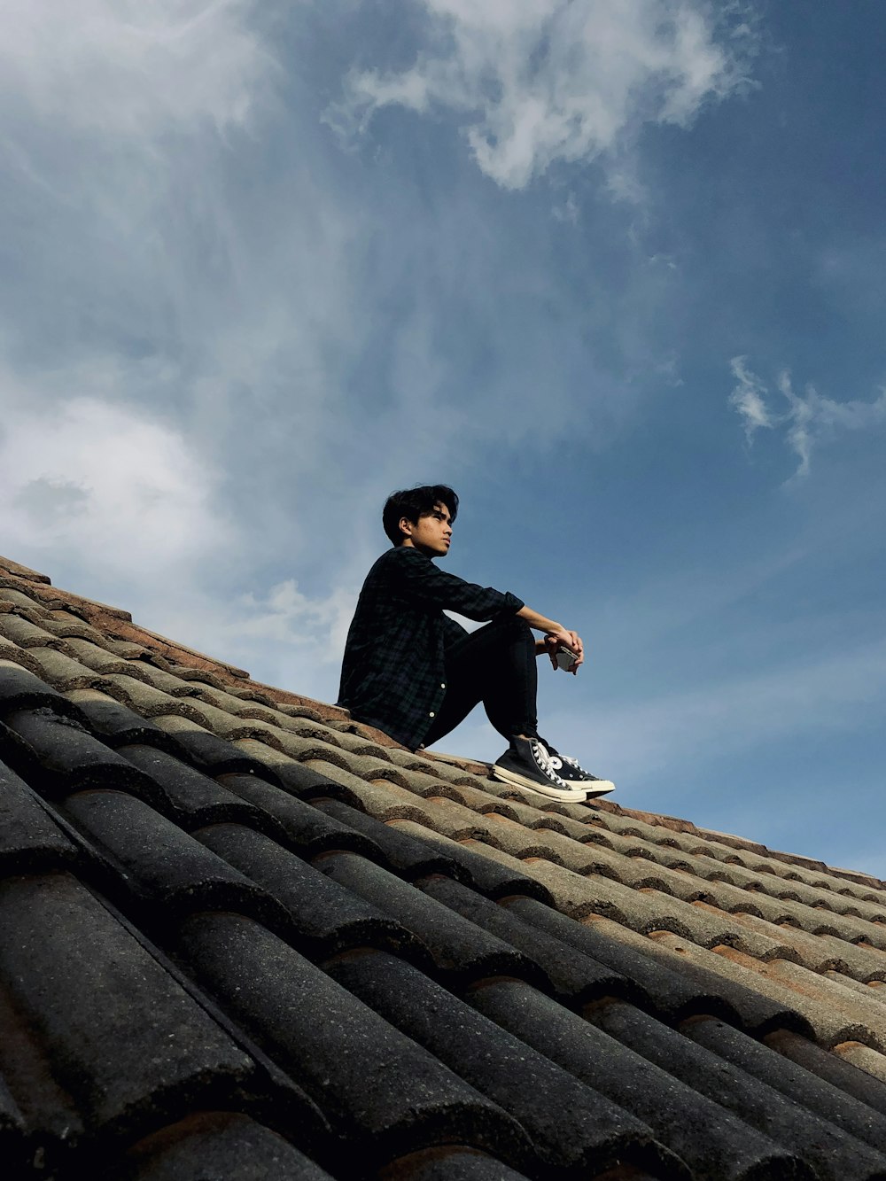 낮 동안 푸른 하늘 아래 지붕에 �앉아 검은 재킷을 입은 남자