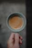 Close-up of a hand holding a rustic, hand-thrown stoneware mug filled with steaming coffee.
