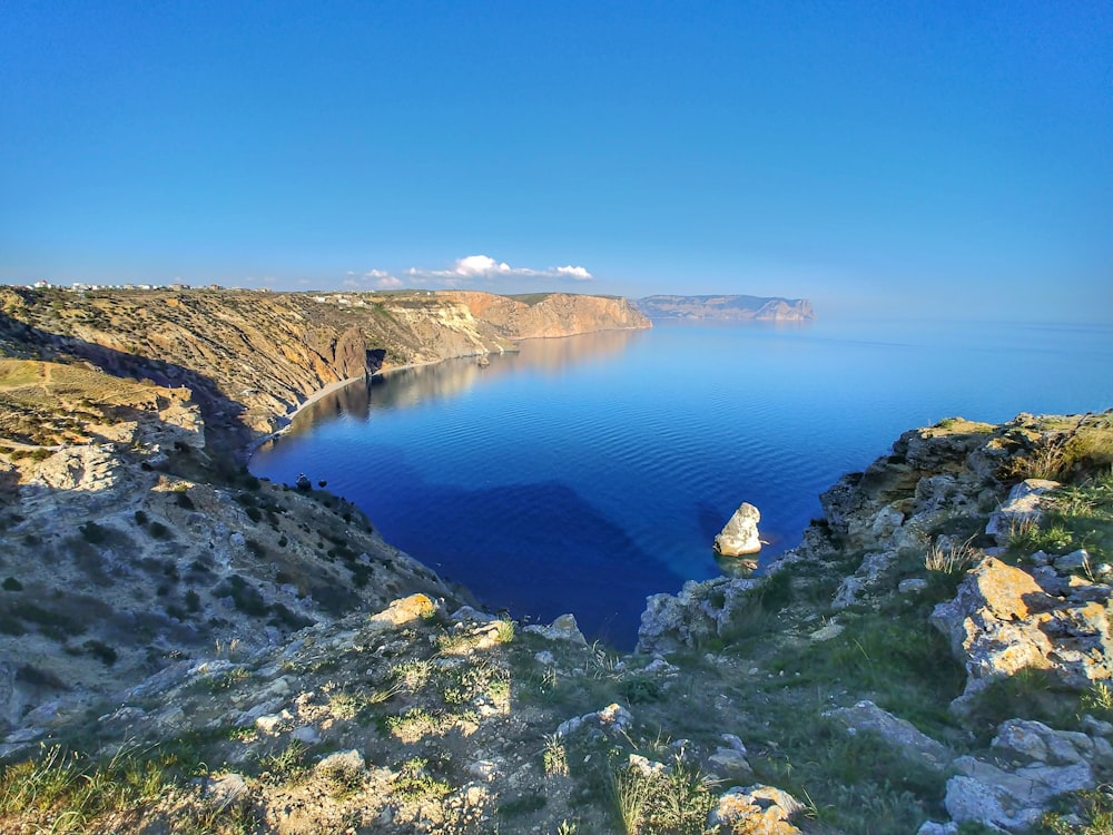 montanha verde e marrom ao lado do lago azul sob o céu azul durante o dia