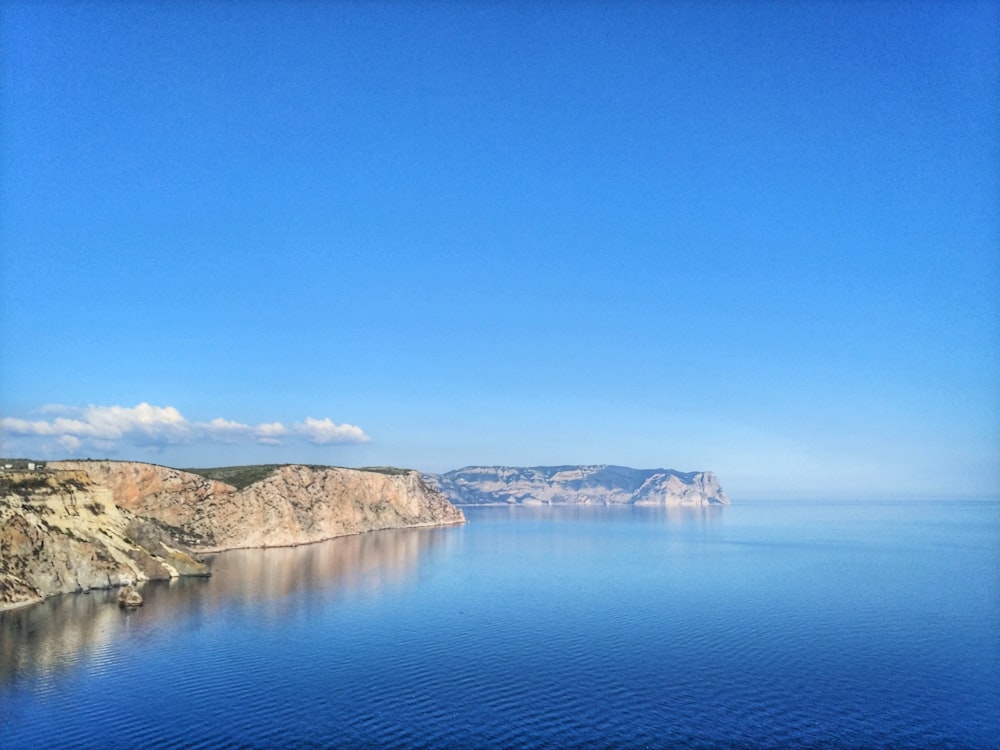 body of water near mountain under blue sky during daytime