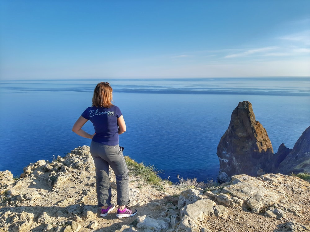 woman in black shirt and brown pants standing on rocky shore during daytime