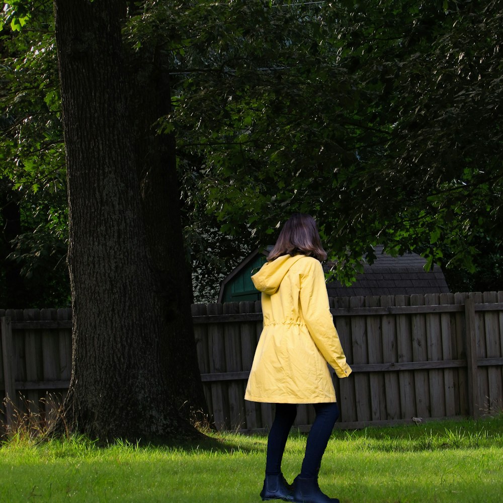 woman in yellow coat standing on green grass field