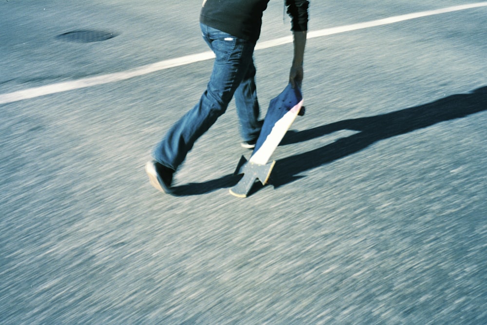 person in blue denim jeans and black jacket walking on gray asphalt road during daytime