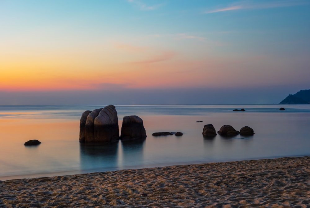 brown rock formation on body of water during sunset