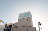 A large building topped with a billboard displaying the word 'Value' in stylized blue and white text. The sky is clear and slightly illuminated by the setting or rising sun. A streetlamp is visible on the left, with utility poles and wires on the right.