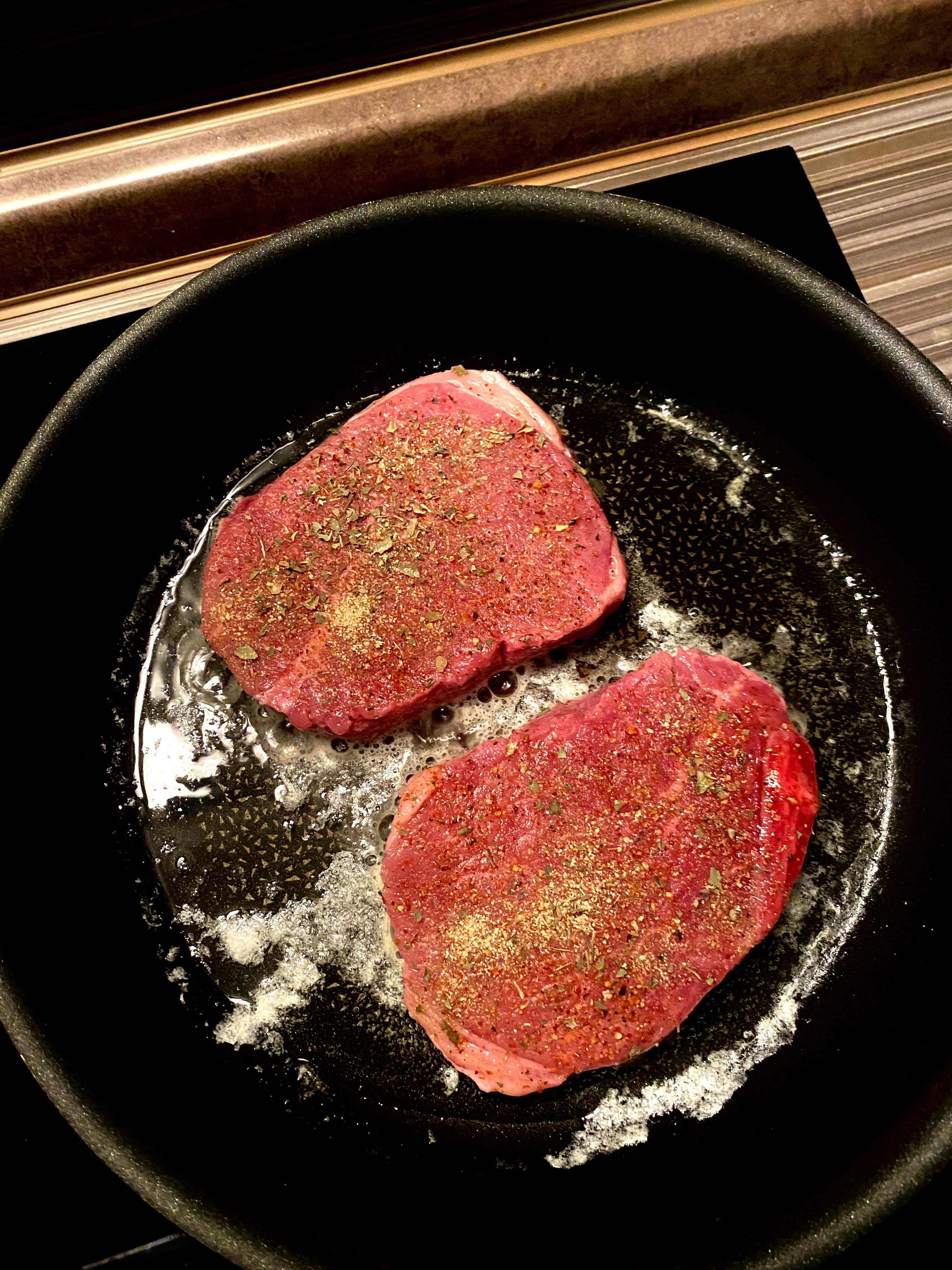 Two seasoned steaks frying in a cast iron skillet.