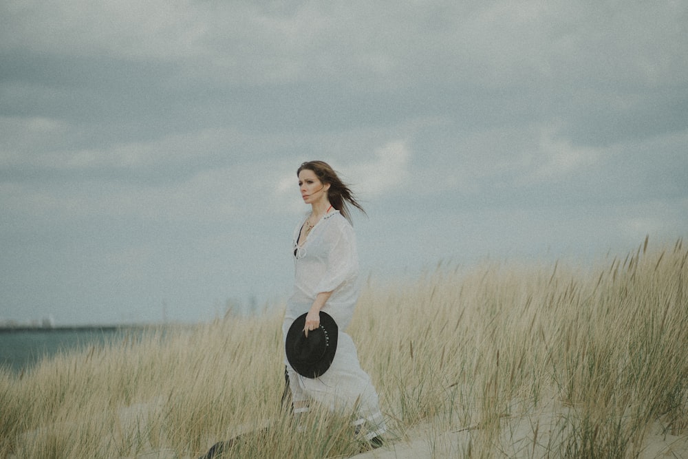 femme en chemise à manches longues blanche et pantalon noir debout sur le champ d’herbe verte sous gris