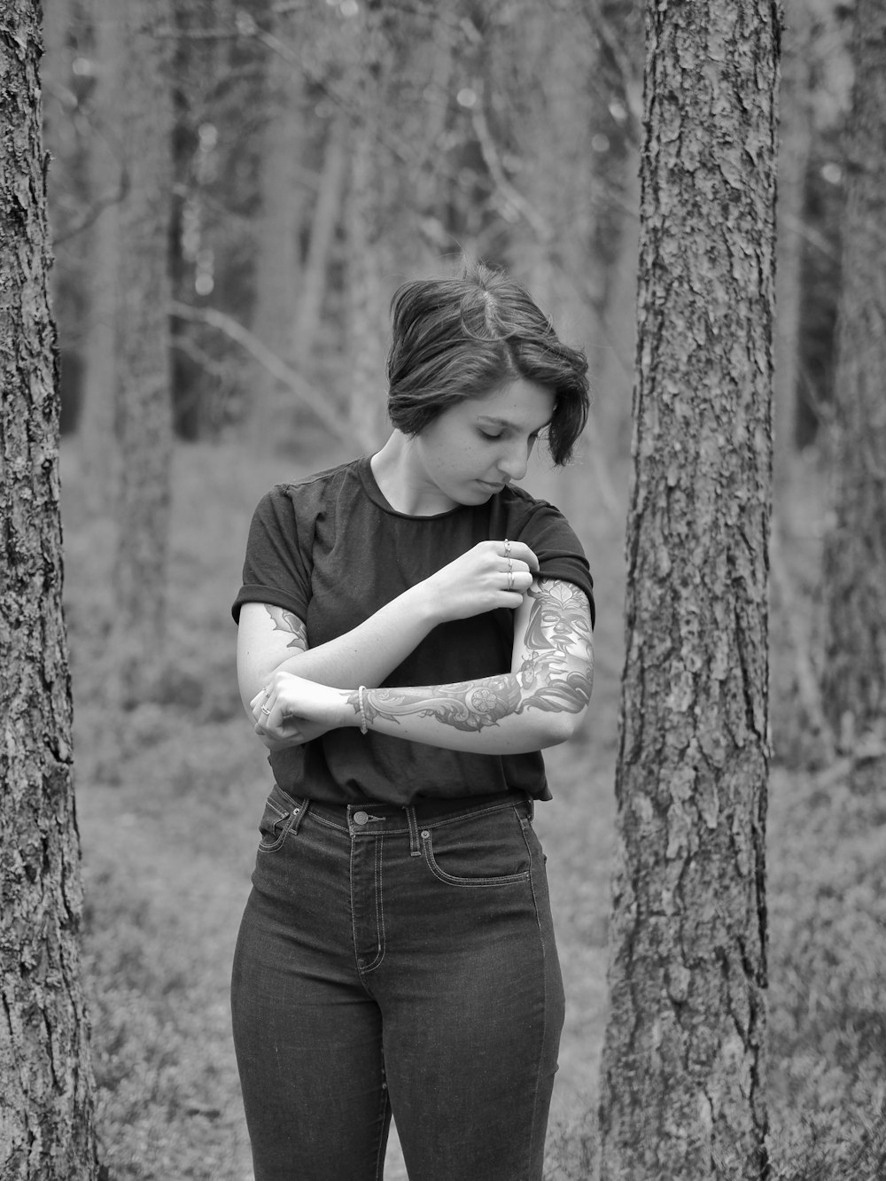 grayscale photo of woman in tank top and denim jeans hugging tree