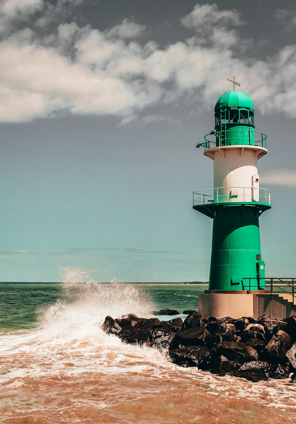 farol verde e branco na formação rochosa marrom ao lado do mar durante o dia