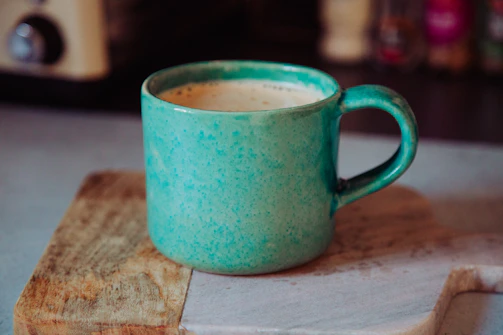 A vibrant hand-thrown ceramic mug in bright turquoise with a cozy knitted background.
