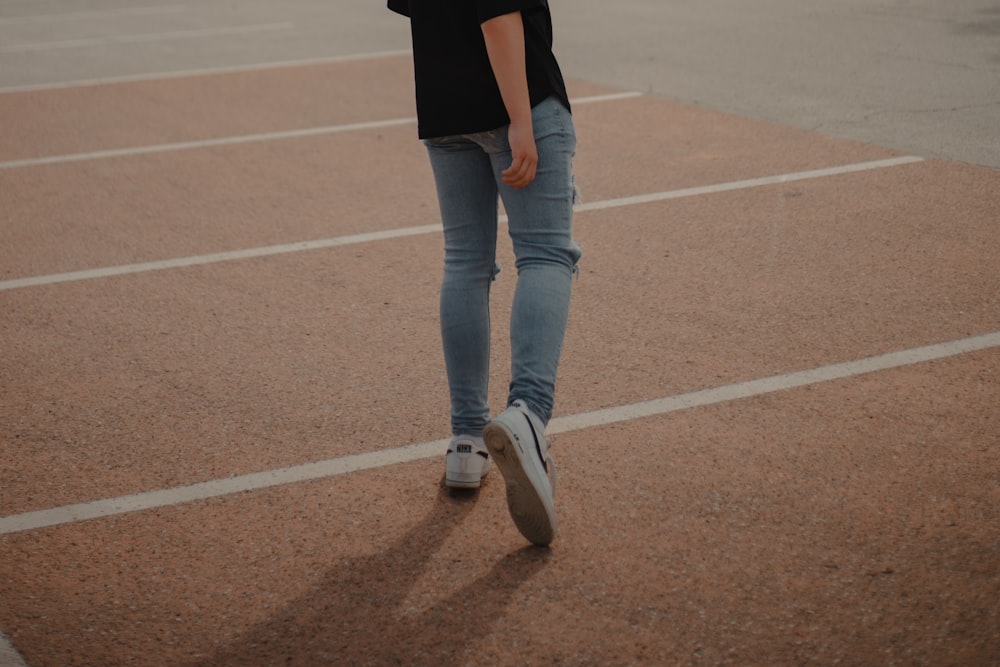 woman in black shirt and blue denim jeans walking on brown field during daytime