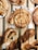 Freshly baked pastries are arranged on a wooden tray, featuring swirls with chocolate and icing drizzles on top. The pastries are golden brown with a flaky texture, and some are twisted in shape, looking crisp and inviting.