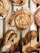 Freshly baked pastries are arranged on a wooden tray, featuring swirls with chocolate and icing drizzles on top. The pastries are golden brown with a flaky texture, and some are twisted in shape, looking crisp and inviting.