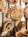 Freshly baked pastries are arranged on a wooden tray, featuring swirls with chocolate and icing drizzles on top. The pastries are golden brown with a flaky texture, and some are twisted in shape, looking crisp and inviting.