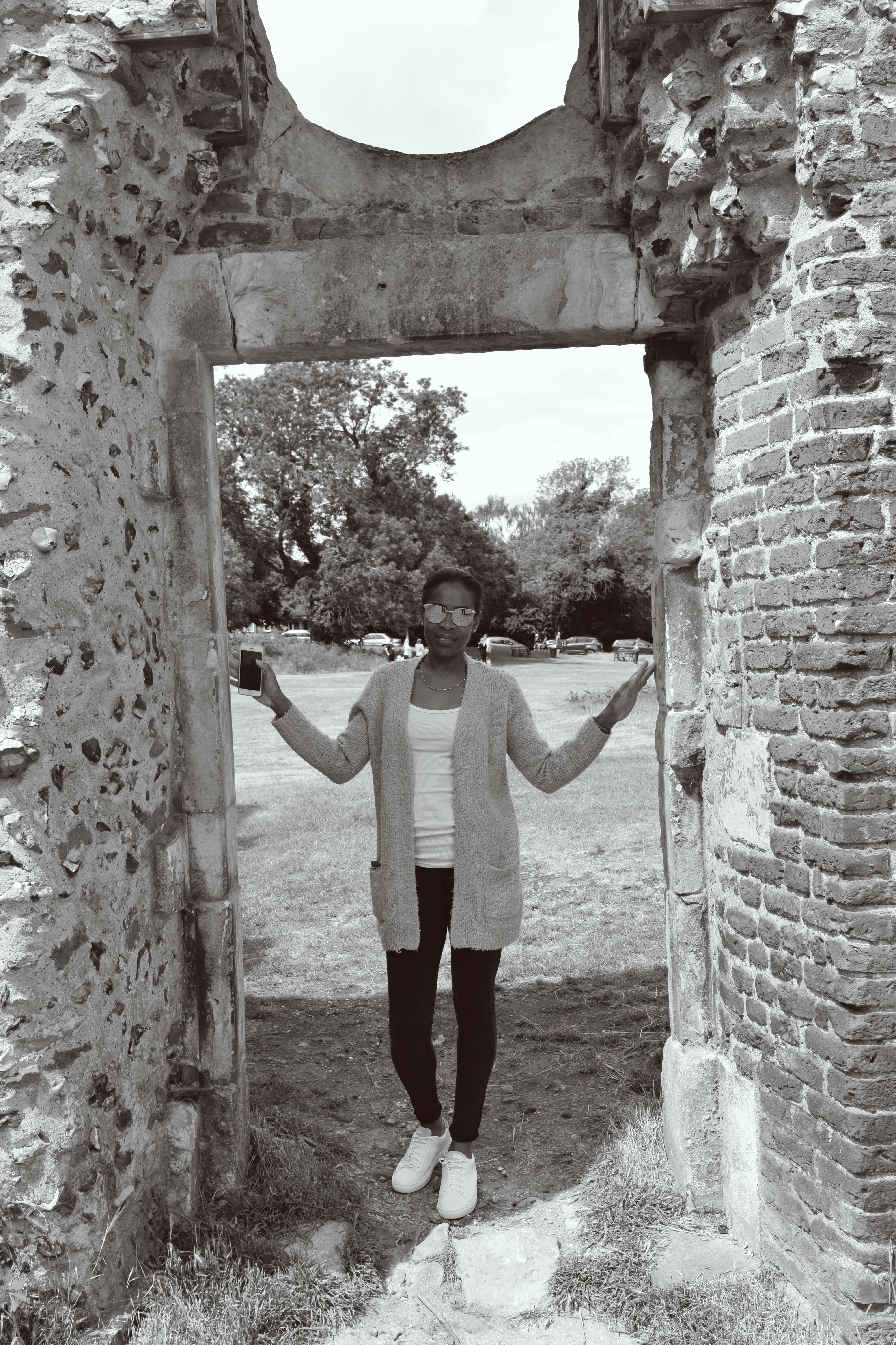 Mujer con camisa blanca de manga larga y pantalones negros de pie en un arco de hormigón marrón durante el día