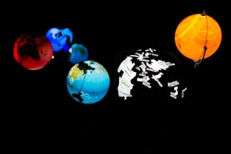 Five planet-like spheres are illuminated against a dark background. The spheres are in various colors: red, blue, orange, and multi-colored with map outlines and corporate names. The arrangement resembles a miniature solar system with each sphere glowing vibrantly.