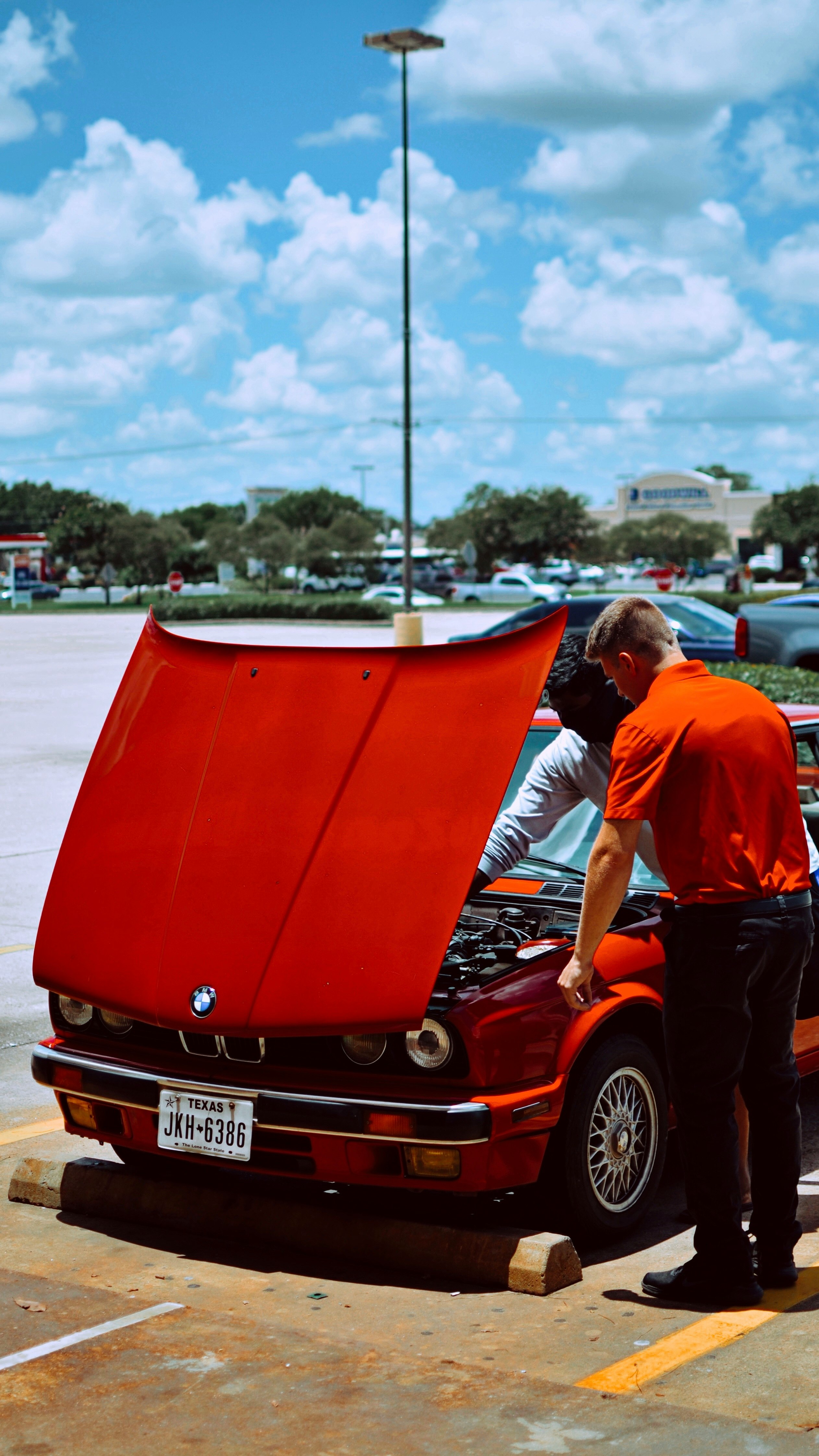 man in blue shirt standing beside red car during daytime