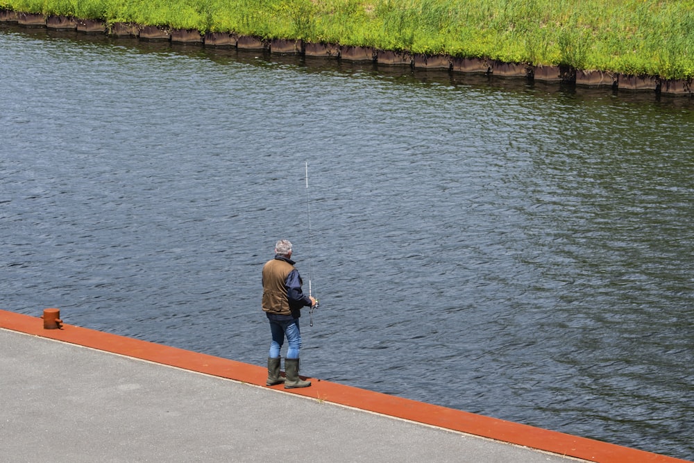 man in gray long sleeve shirt and blue denim jeans standing on concrete dock during daytime