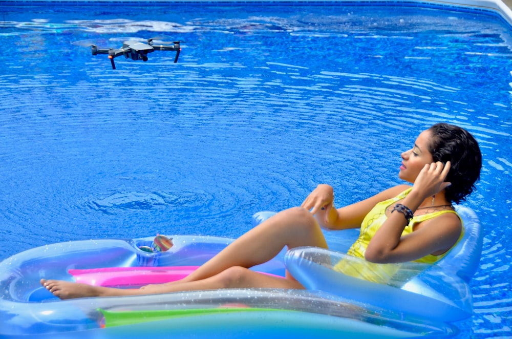 노란색 비키니를 입은 여자는 낮 동안 푸른 물에 분홍색과 파란색 풍선 플로트에 누워 있습니다.