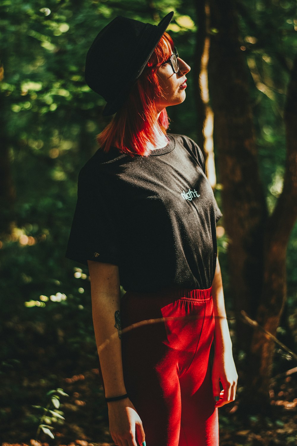 Mujer con camiseta negra de cuello redondo y falda roja de pie cerca de árboles verdes durante el día