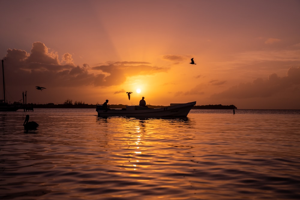 silhouette of 2 people riding on boat during sunset