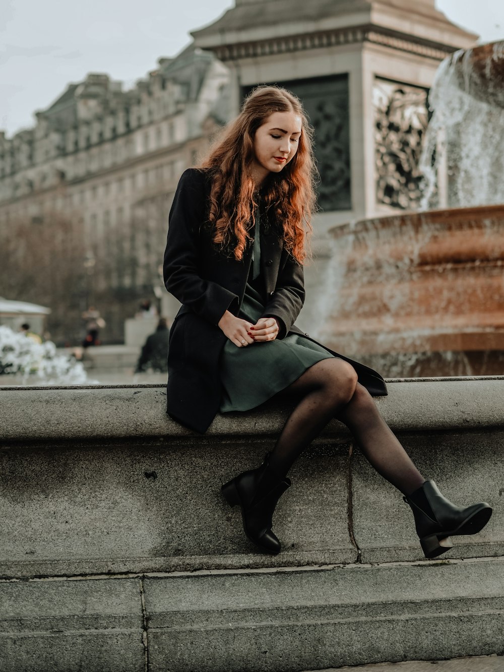 woman in black coat sitting on concrete bench during daytime