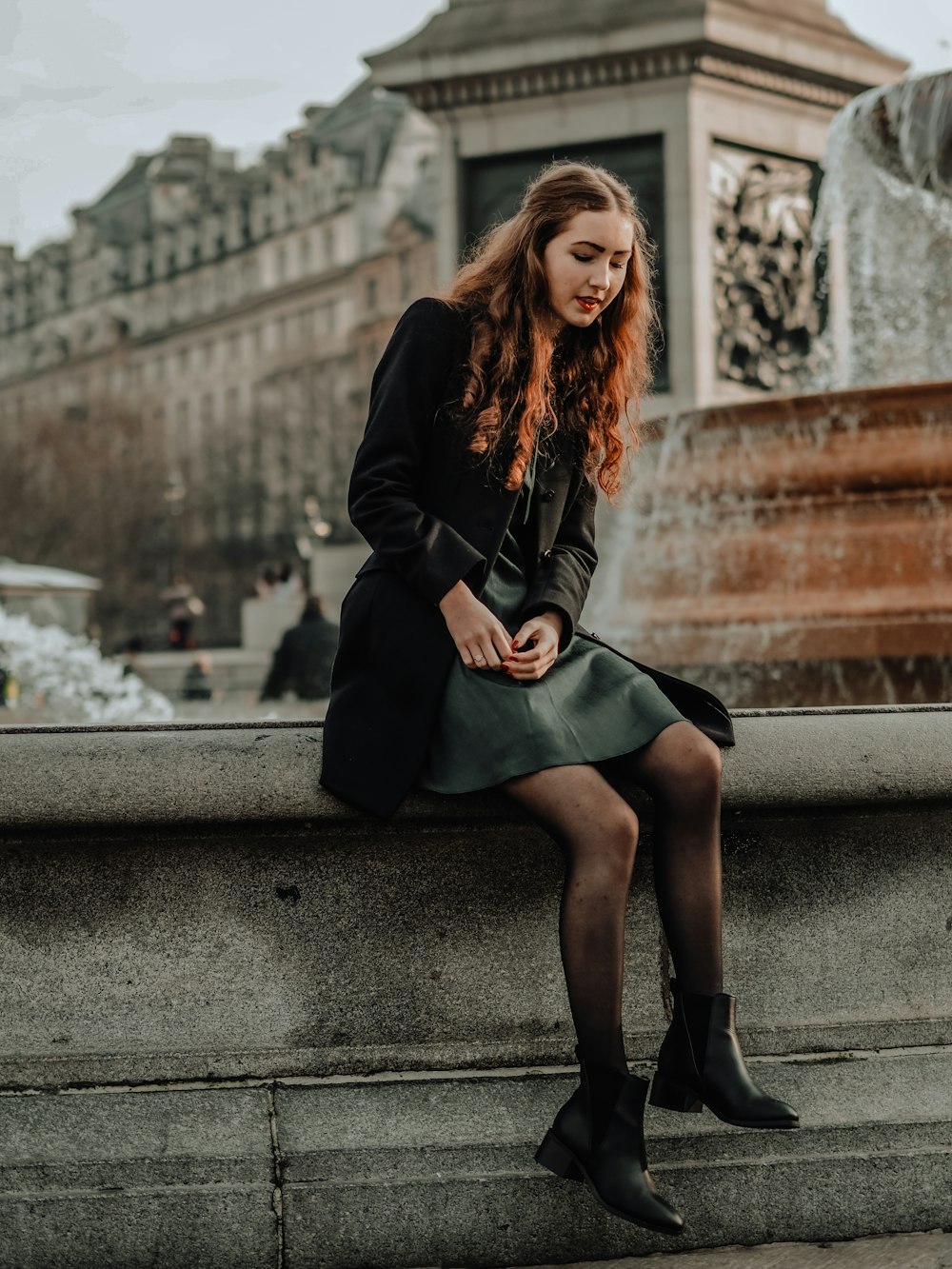 woman in black long sleeve dress sitting on gray concrete bench during daytime