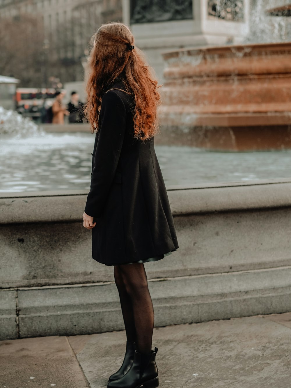 donna in cappotto nero in piedi sul ponte concreto durante il giorno