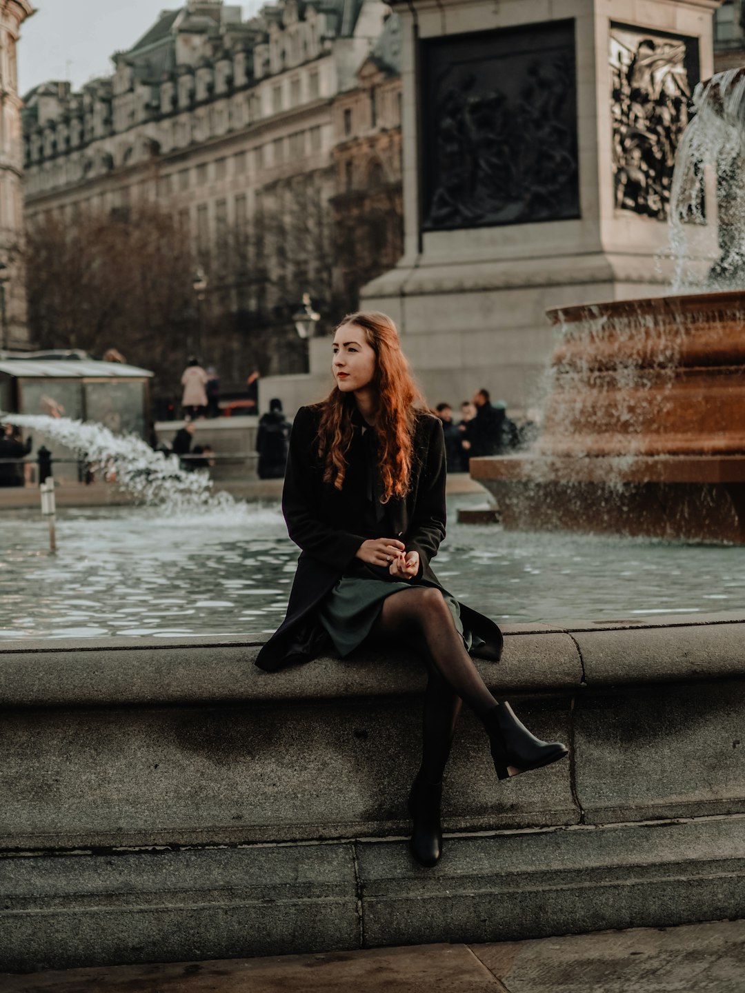 woman in black dress sitting on water fountain during daytime