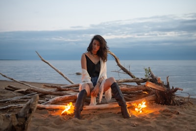 woman in white tank top sitting on brown log near bonfire during daytime bonfire teams background