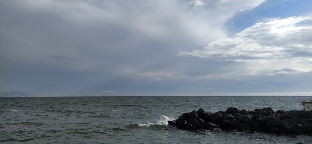 black rocks on sea under white clouds and blue sky during daytime