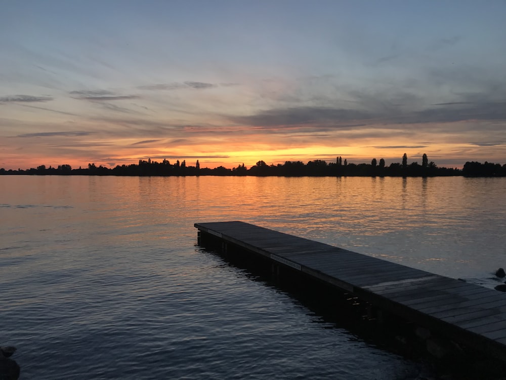 brown wooden dock on body of water during sunset