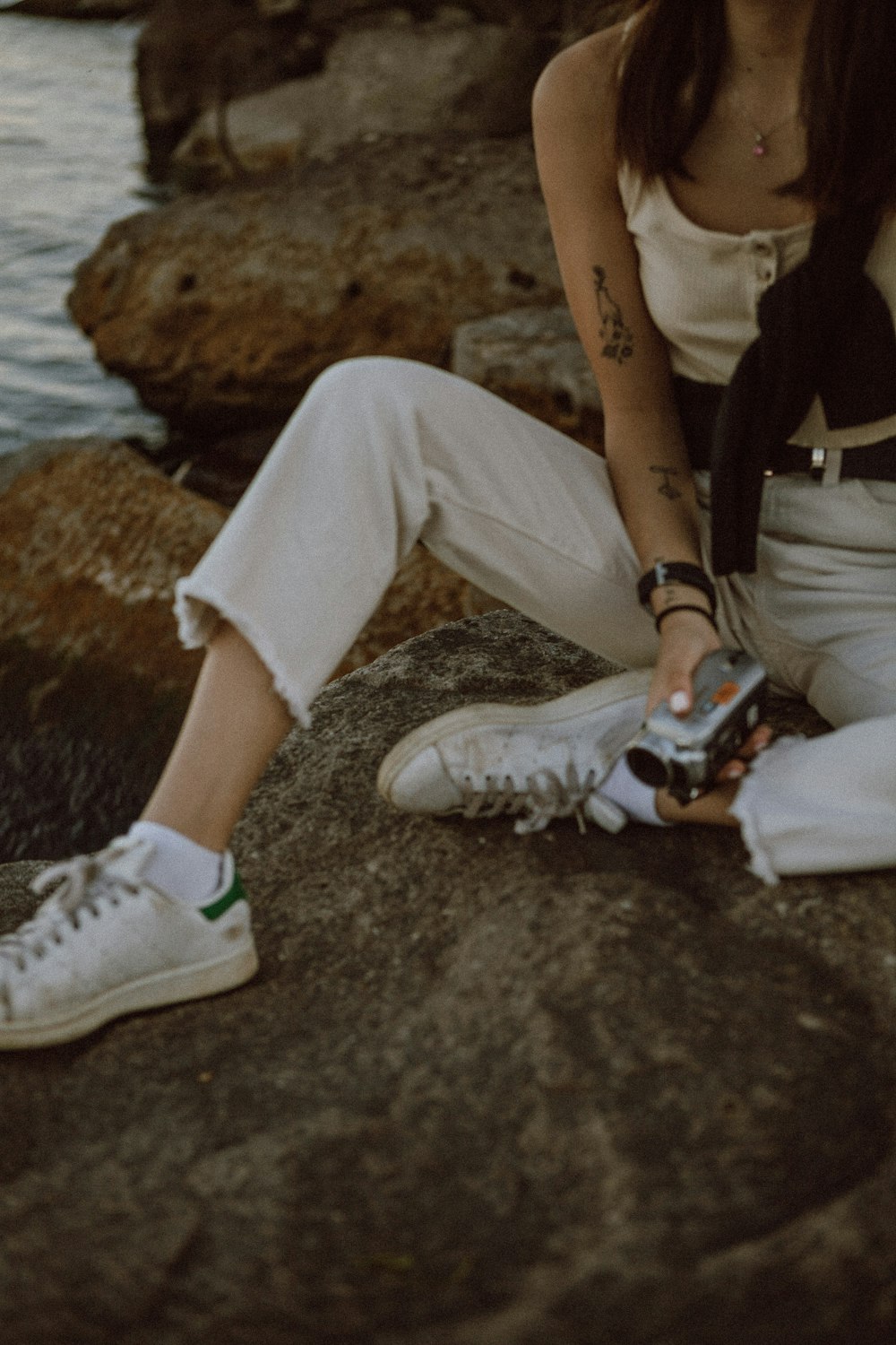 person in white pants and white nike sneakers sitting on rock