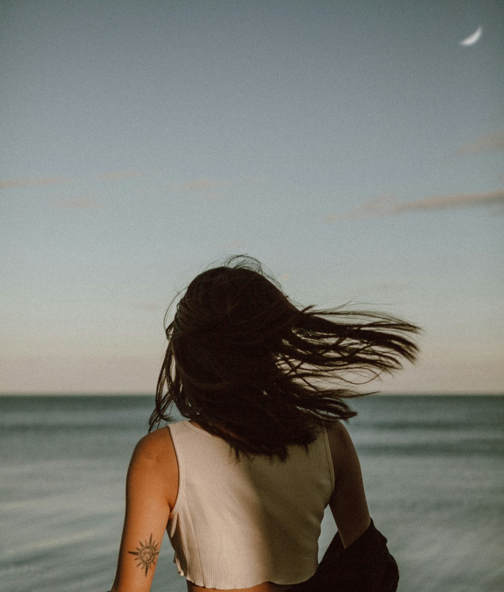 femme en débardeur blanc debout sur la plage pendant la journée