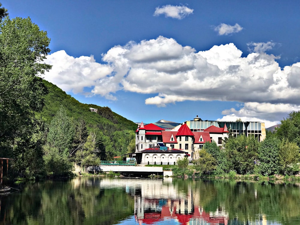 white and red concrete house beside lake under blue sky and white clouds during daytime