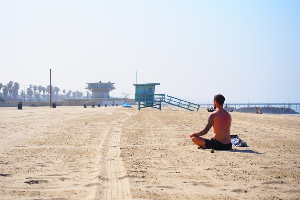man in black shorts sitting on beach during daytime