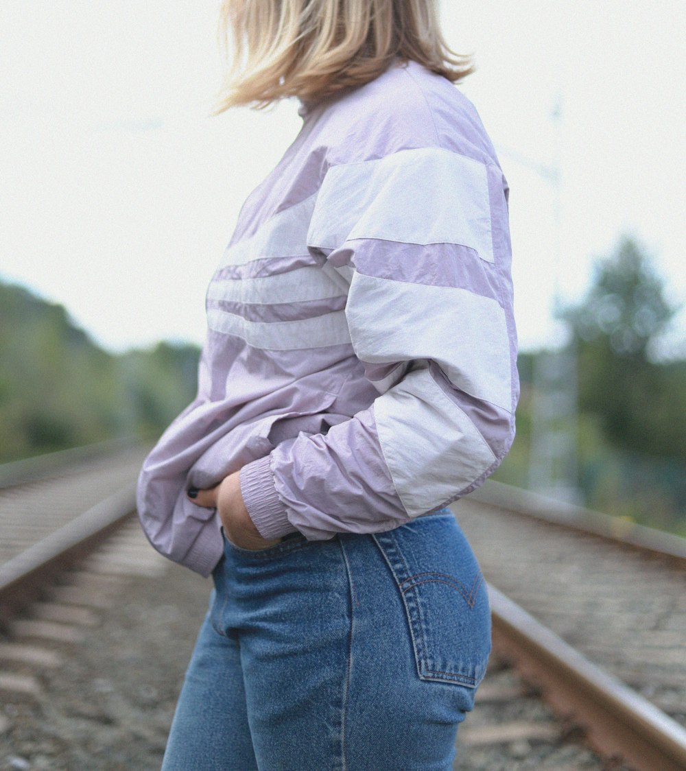 woman in pink long sleeve shirt and blue denim jeans standing on brown wooden bridge during