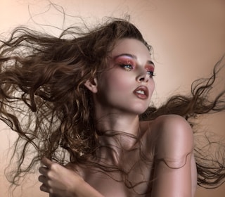 A bold and glamorous makeup look paired with voluminous, styled hair against a neutral background.