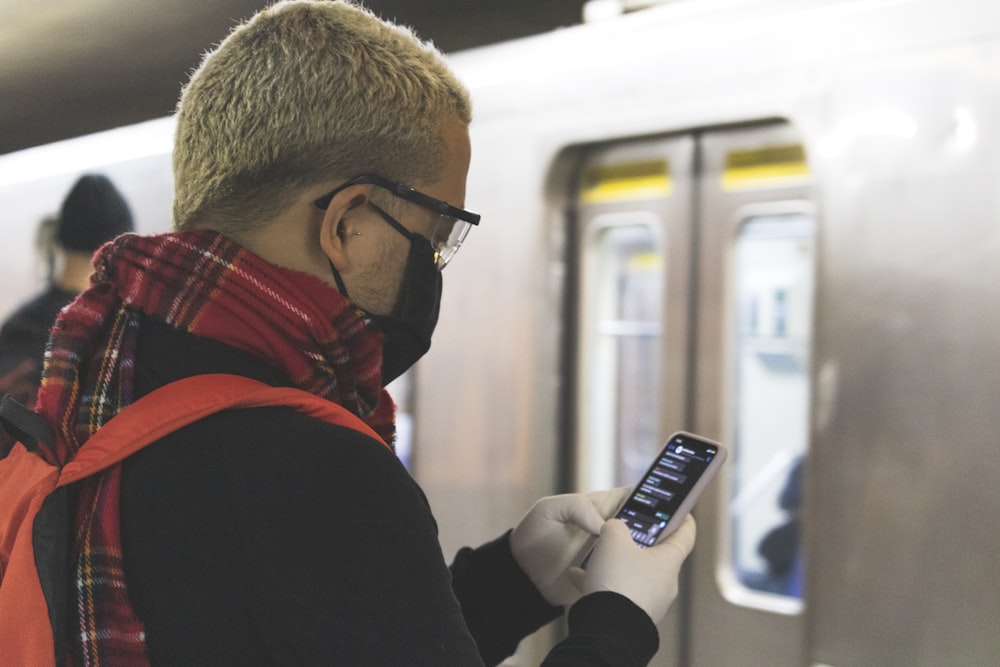 man in black and red jacket wearing black framed eyeglasses holding black and white candybar phone