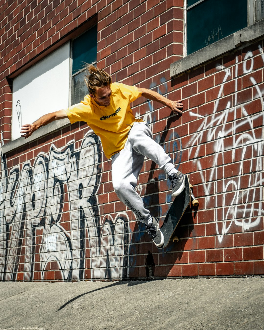 woman in yellow shirt and gray pants jumping on brown brick wall during daytime