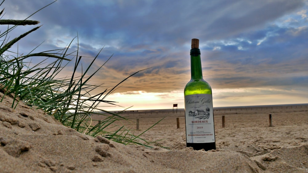 Grüne Glasflasche auf braunem Sand bei Sonnenuntergang