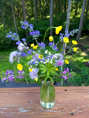 A serene forest backdrop with a ceramic vase holding wildflowers on a stump.