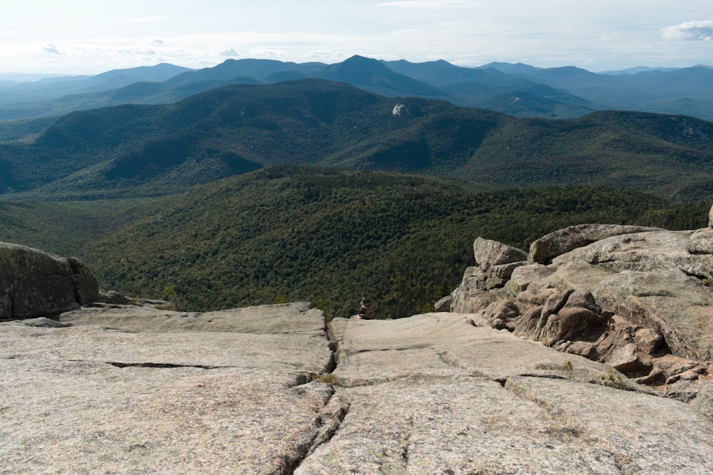 person in blue shirt standing on brown rock near green mountains during daytime