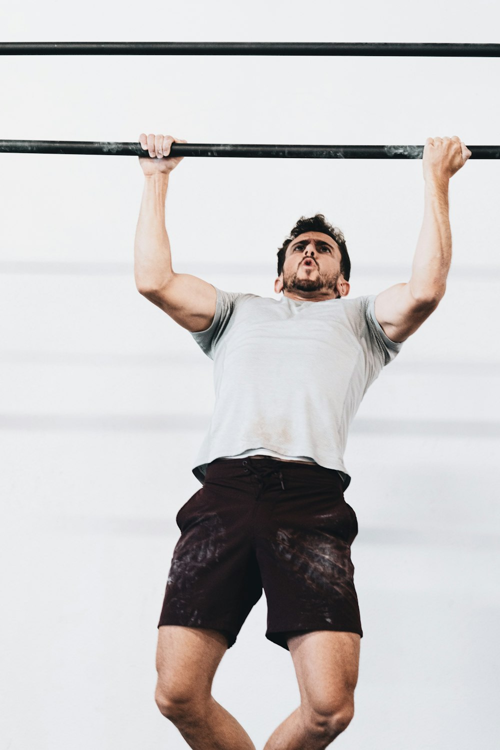 man in white crew neck t-shirt and black shorts holding on gray metal bar