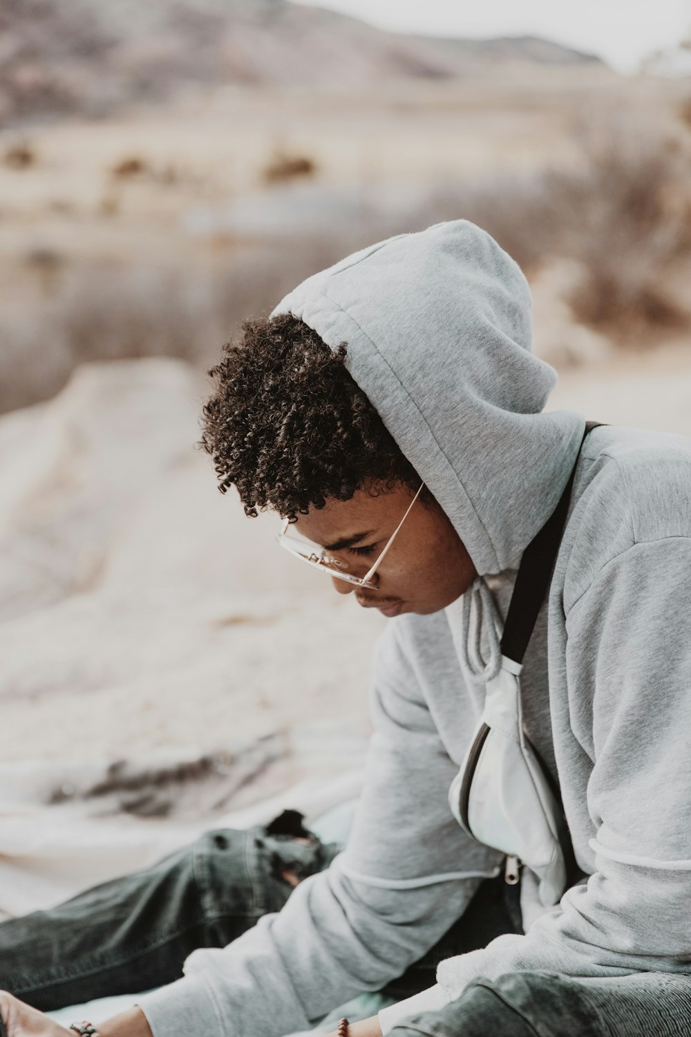 man in gray hoodie sitting on white sand during daytime