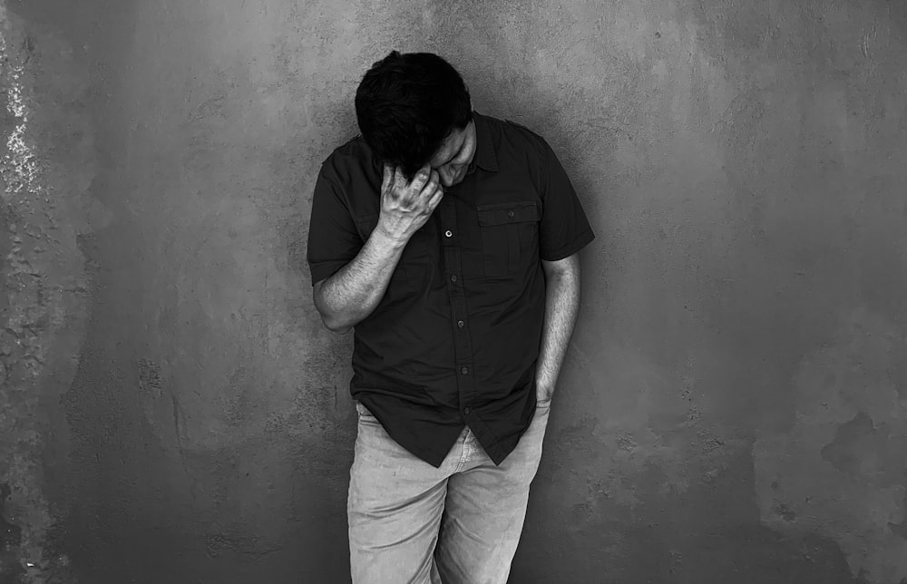 man in black button up shirt and white pants leaning on wall